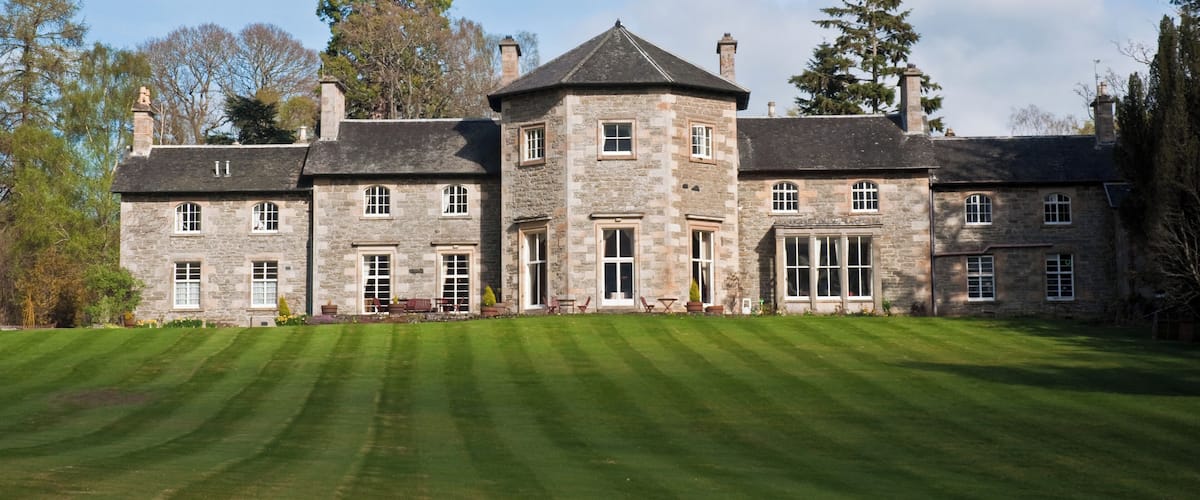 A large stone building with a central tower, surrounded by a well-manicured lawn and tall trees.