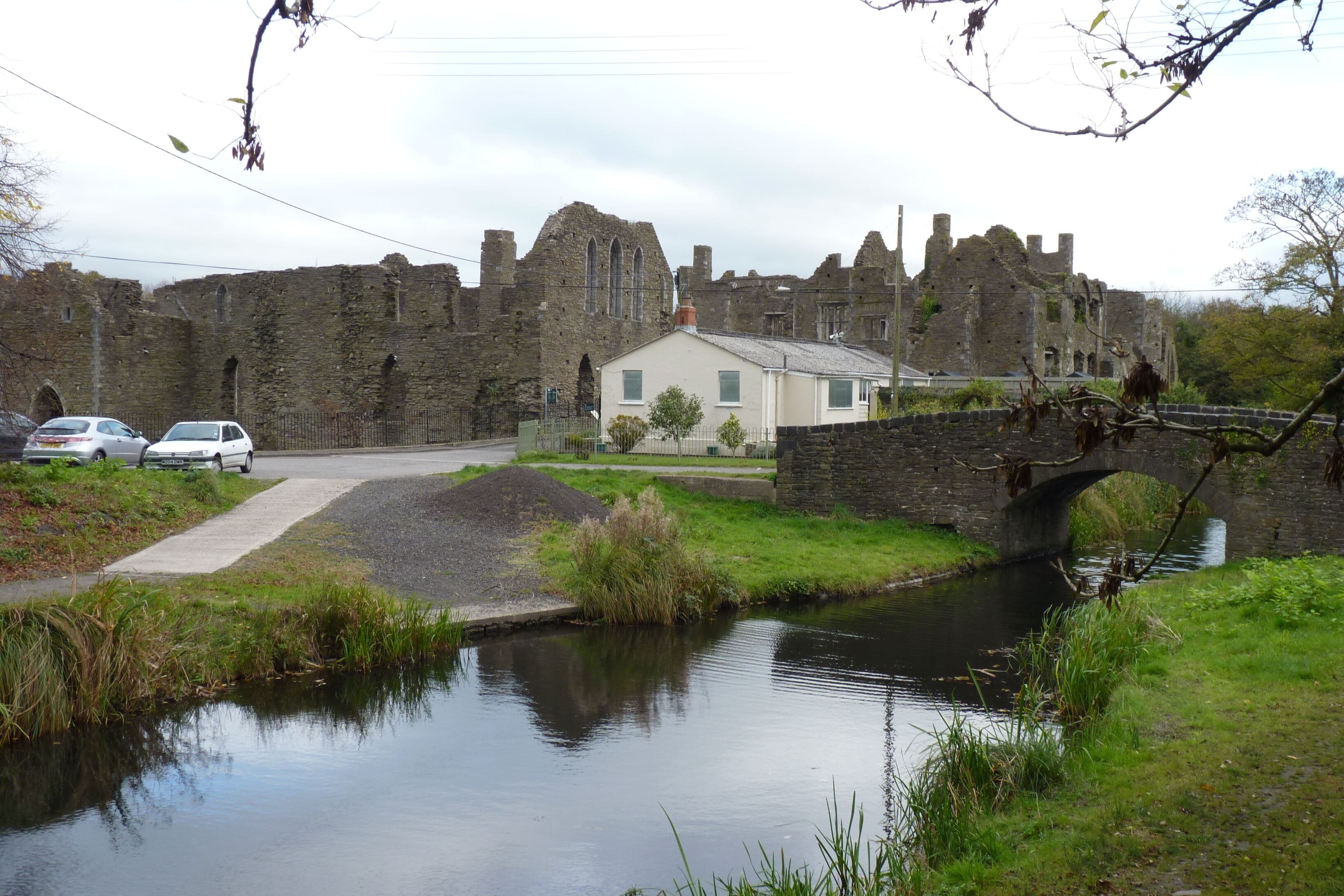 A historic castle with ruins, a small bridge, a canal, and a modern house.