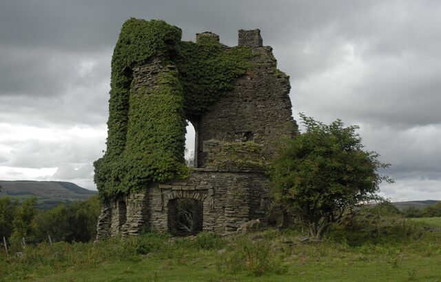 Una estructura de piedra en ruinas con muros cubiertos de hiedra y una única ventana intacta.