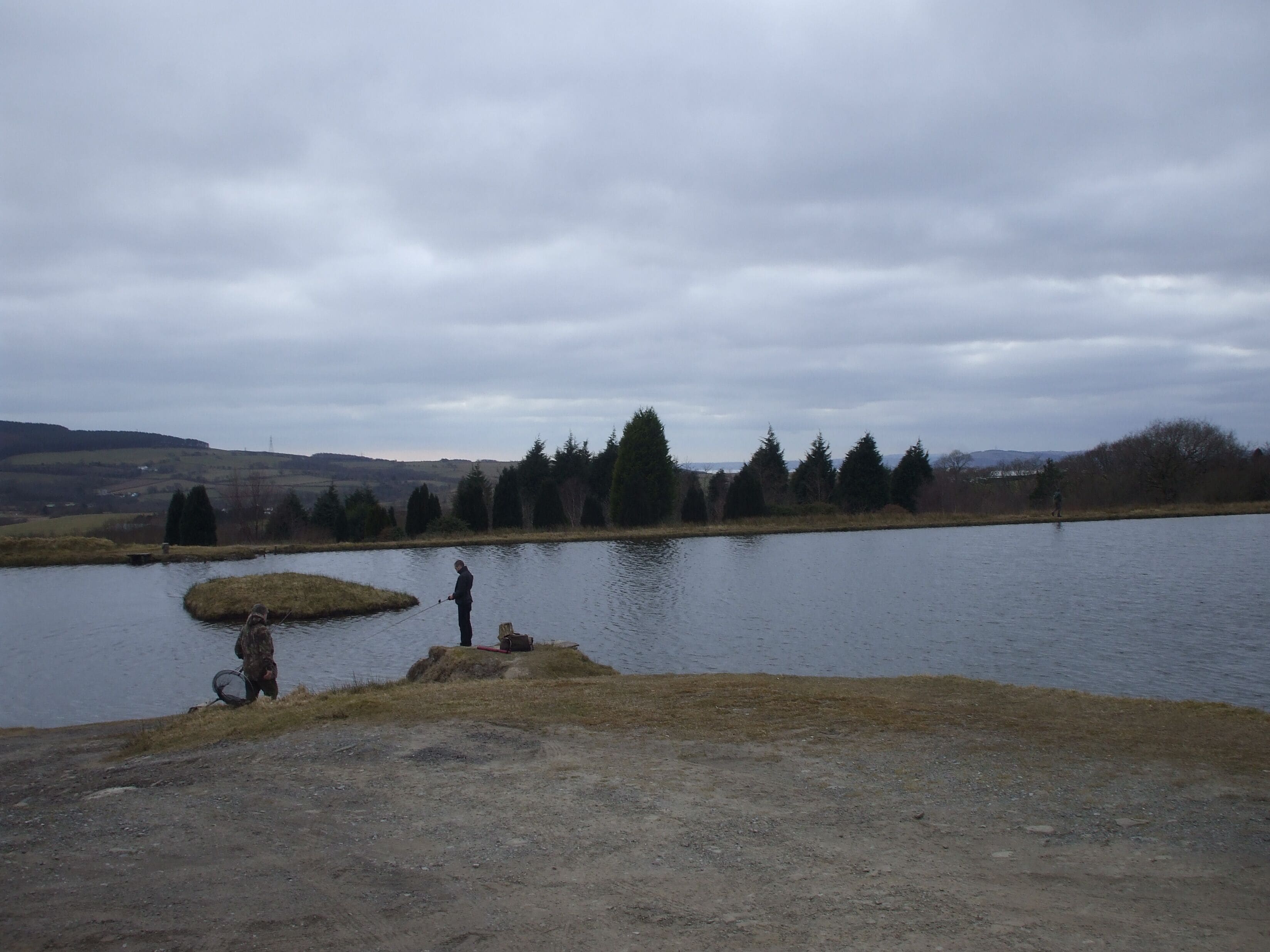 Un lago con una persona pescando, rodeado de árboles y colinas.