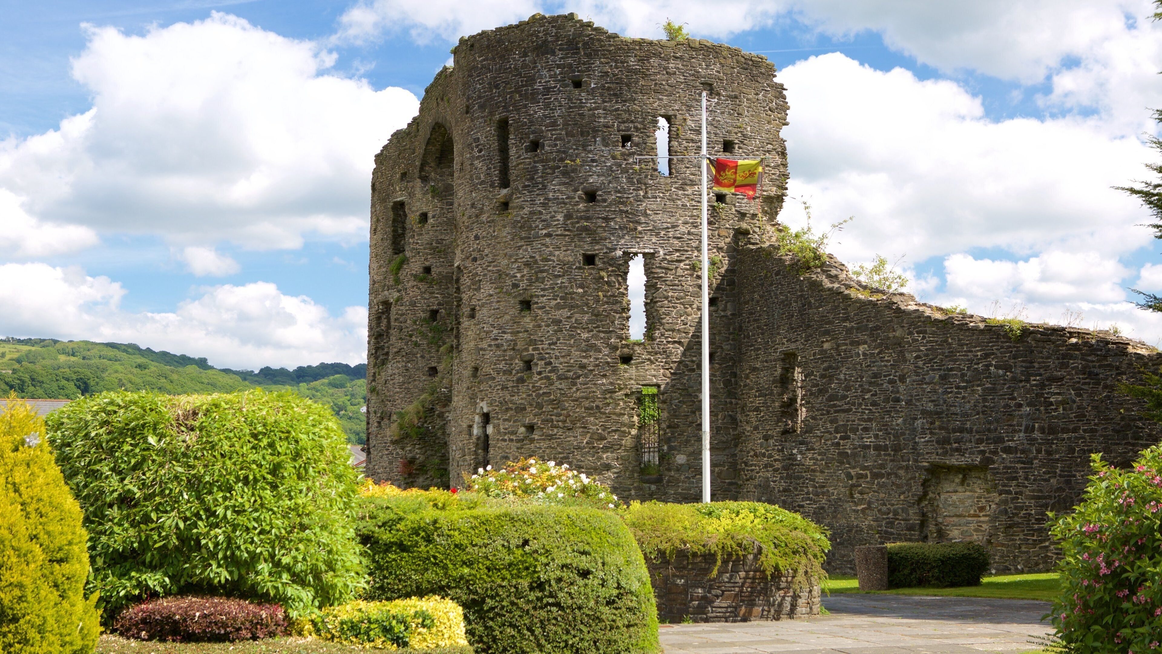 A historic stone tower with a flag, surrounded by well-maintained gardens and a clear sky.