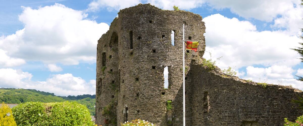 A historic stone tower with a flag, surrounded by well-maintained gardens and a clear sky.