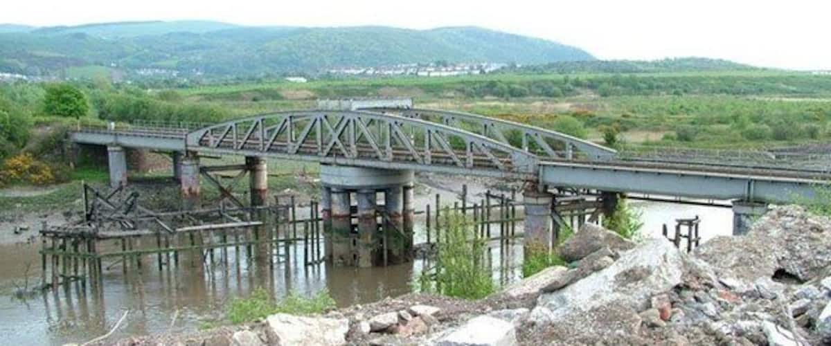 A bridge over a river with a hilly landscape in the background.
