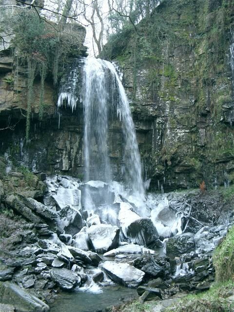 Uma cascata despencando sobre rochas em uma área arborizada.