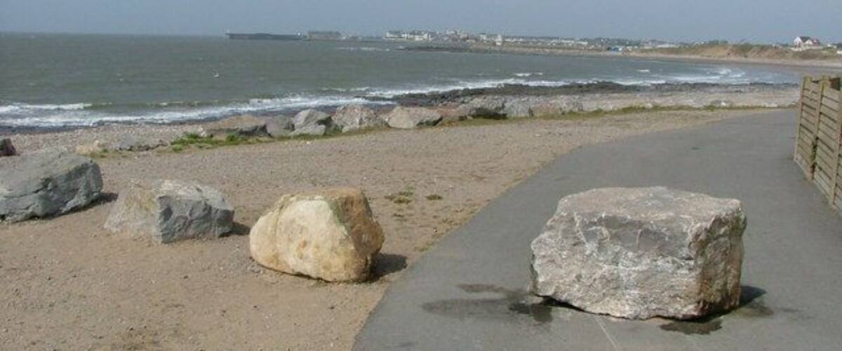 A coastal walkway with large rocks and a view of the sea.