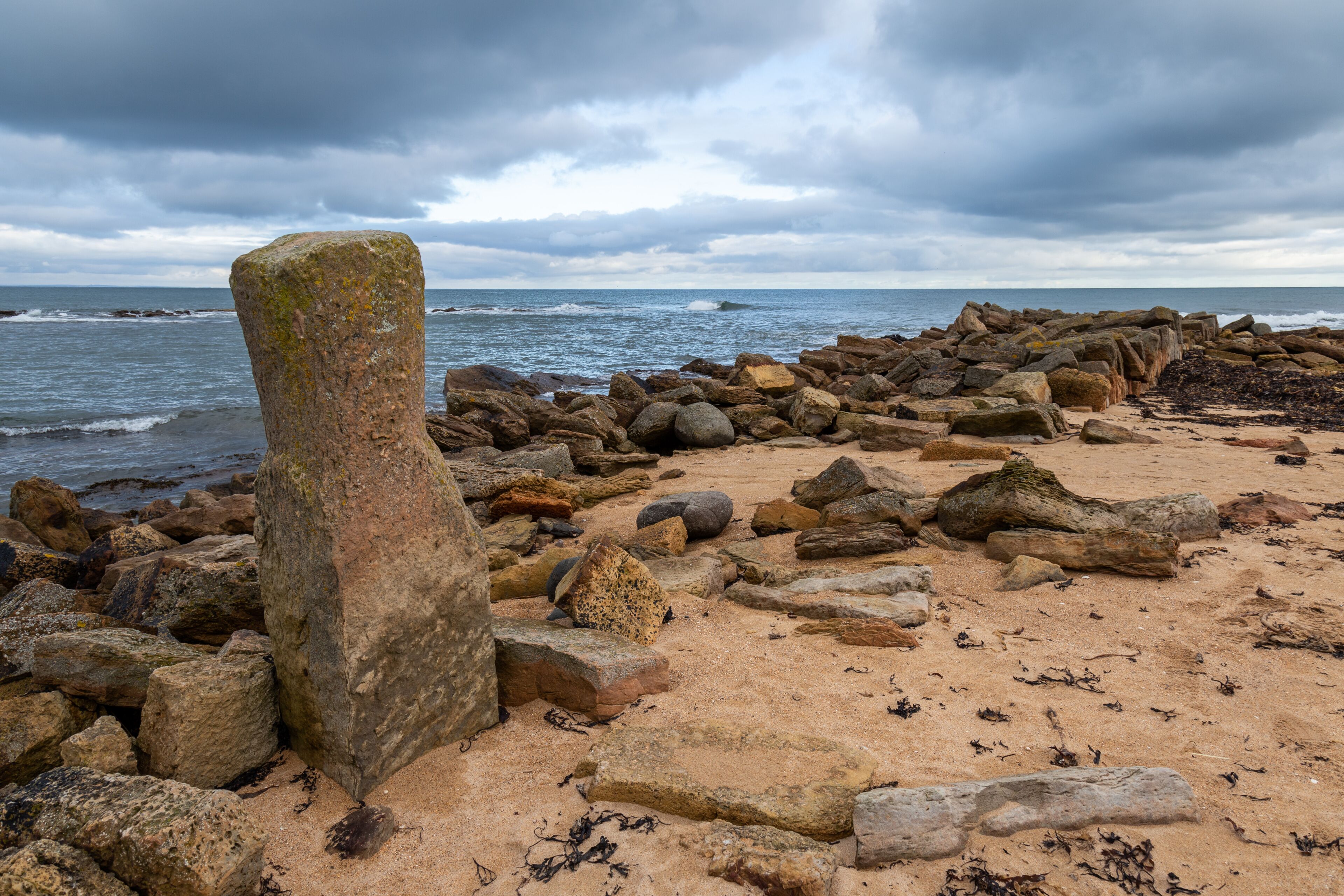 A rocky shoreline with large boulders and a prominent vertical rock formation.