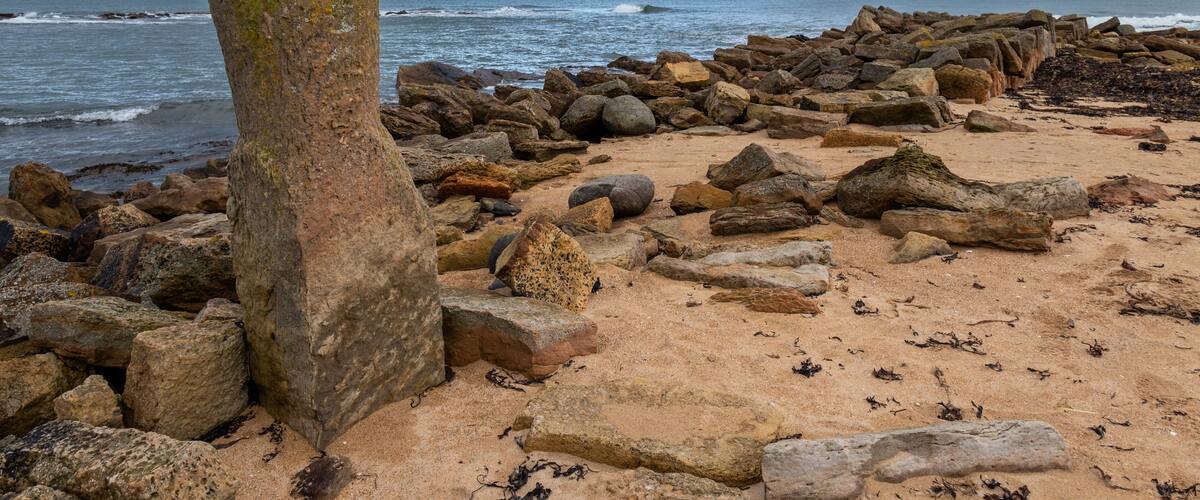 A rocky shoreline with large boulders and a prominent vertical rock formation.