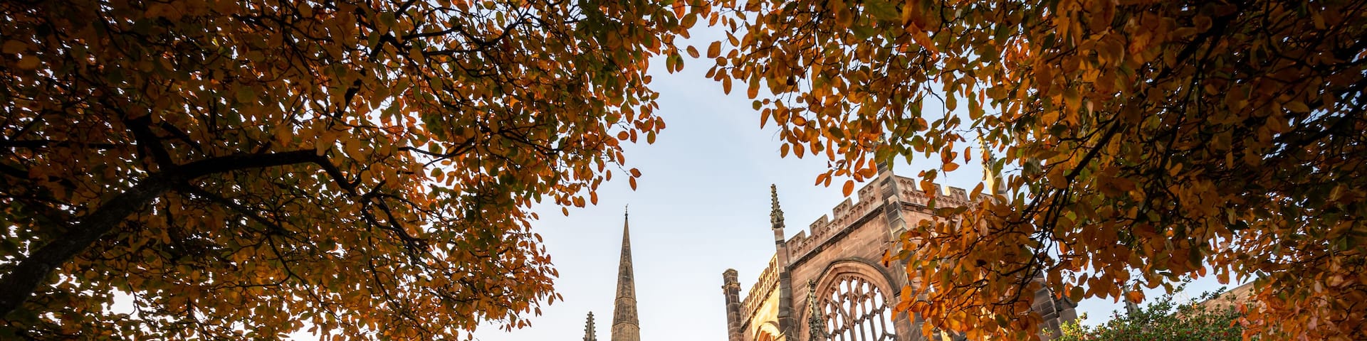 A historic building with Gothic architecture, a cobblestone street, and autumn foliage.