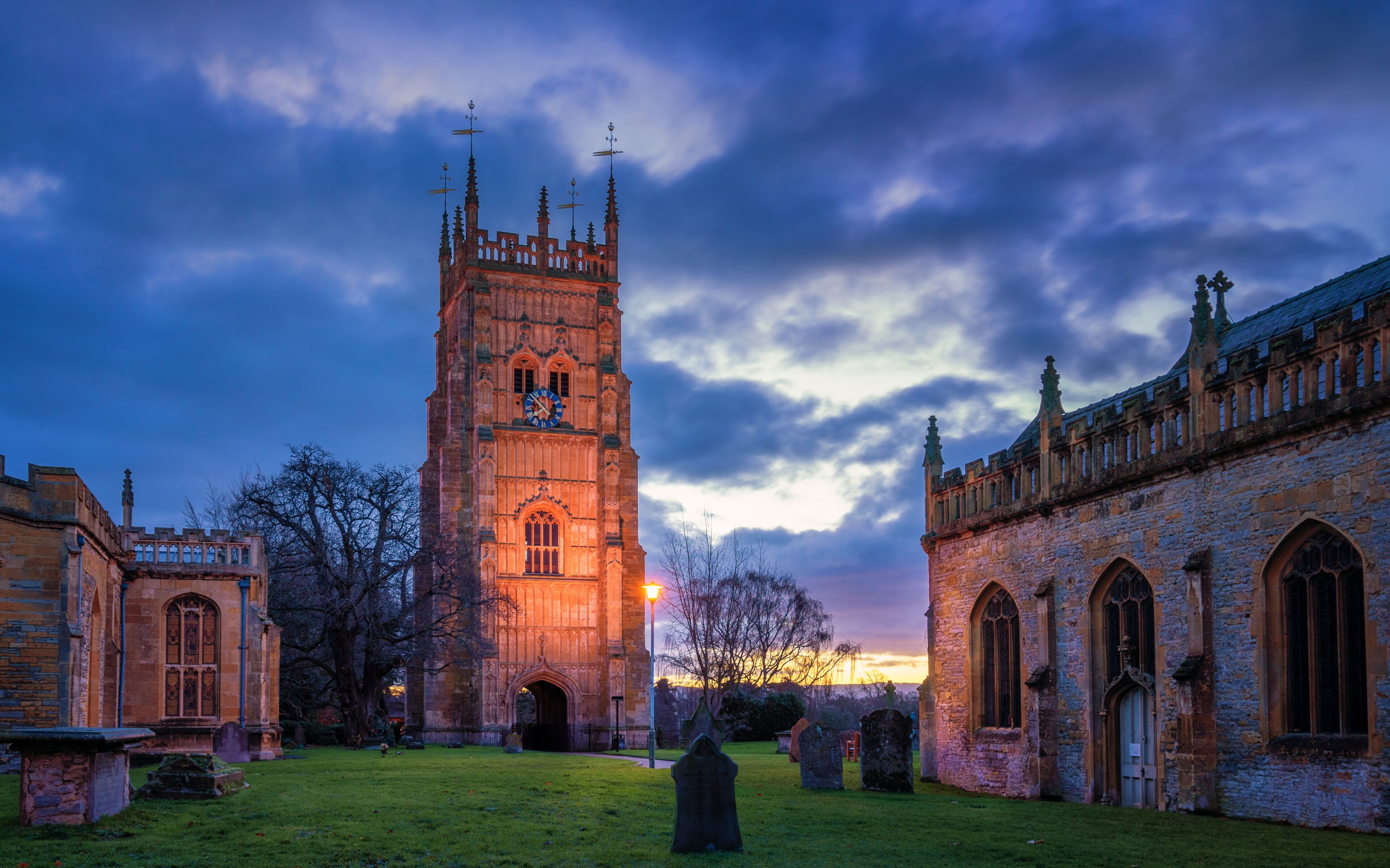A historic tower with a clock, surrounded by ancient buildings and a cemetery.