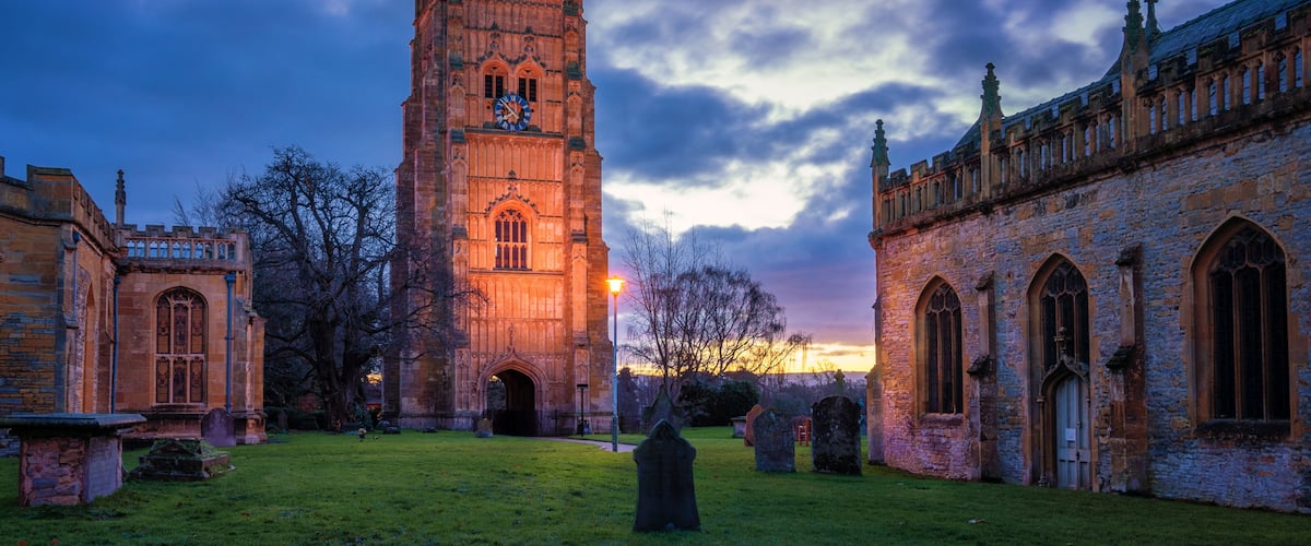 A historic tower with a clock, surrounded by ancient buildings and a cemetery.