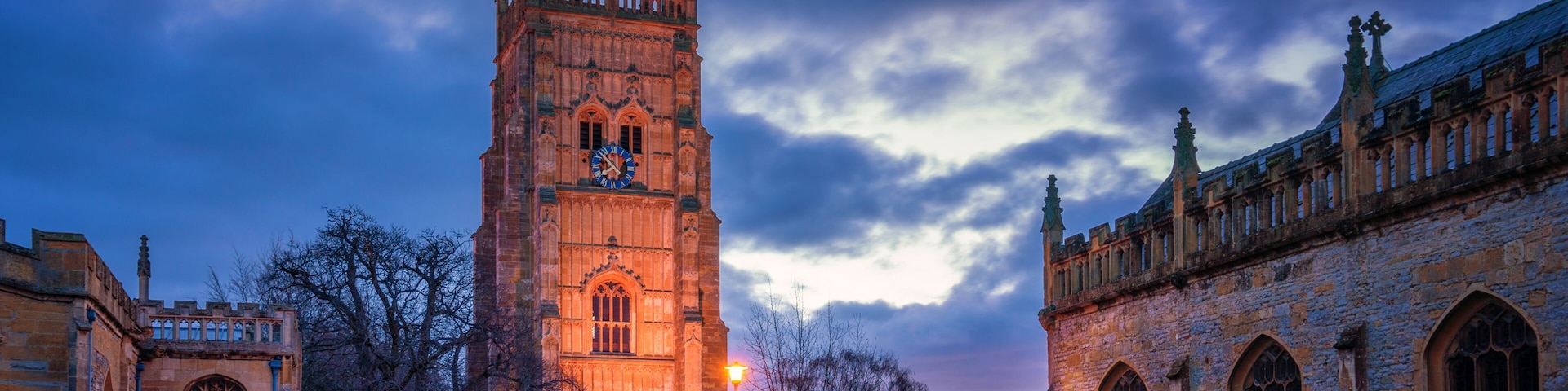 A historic tower with a clock, surrounded by ancient buildings and a cemetery.