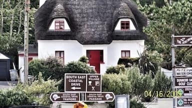 Een huis met een uniek rieten dak en een rode deur, omringd door groen en routeborden.