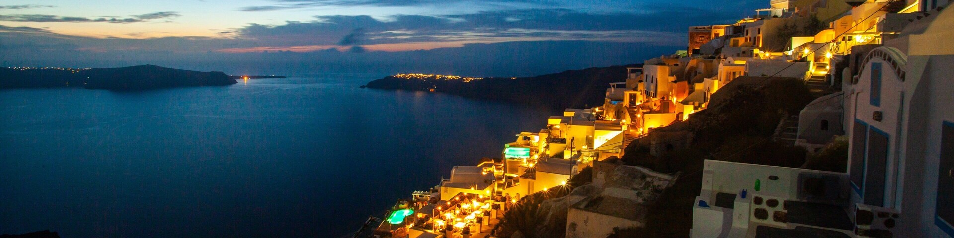 Uma cidade costeira à noite, com edifícios iluminados e vista para o mar.
