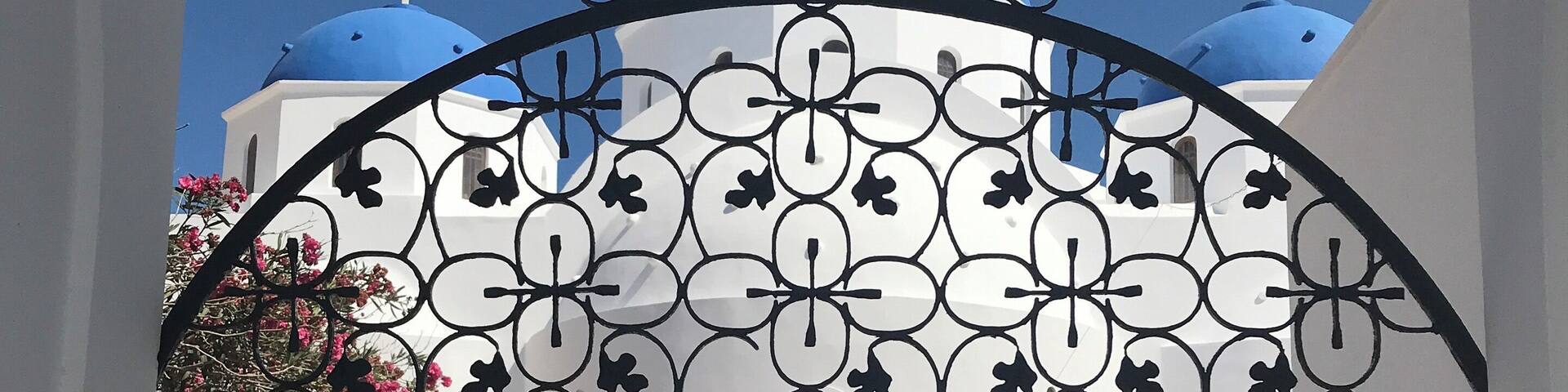 A wrought iron gate with a cross at the top, leading to a building with blue domes and crosses.