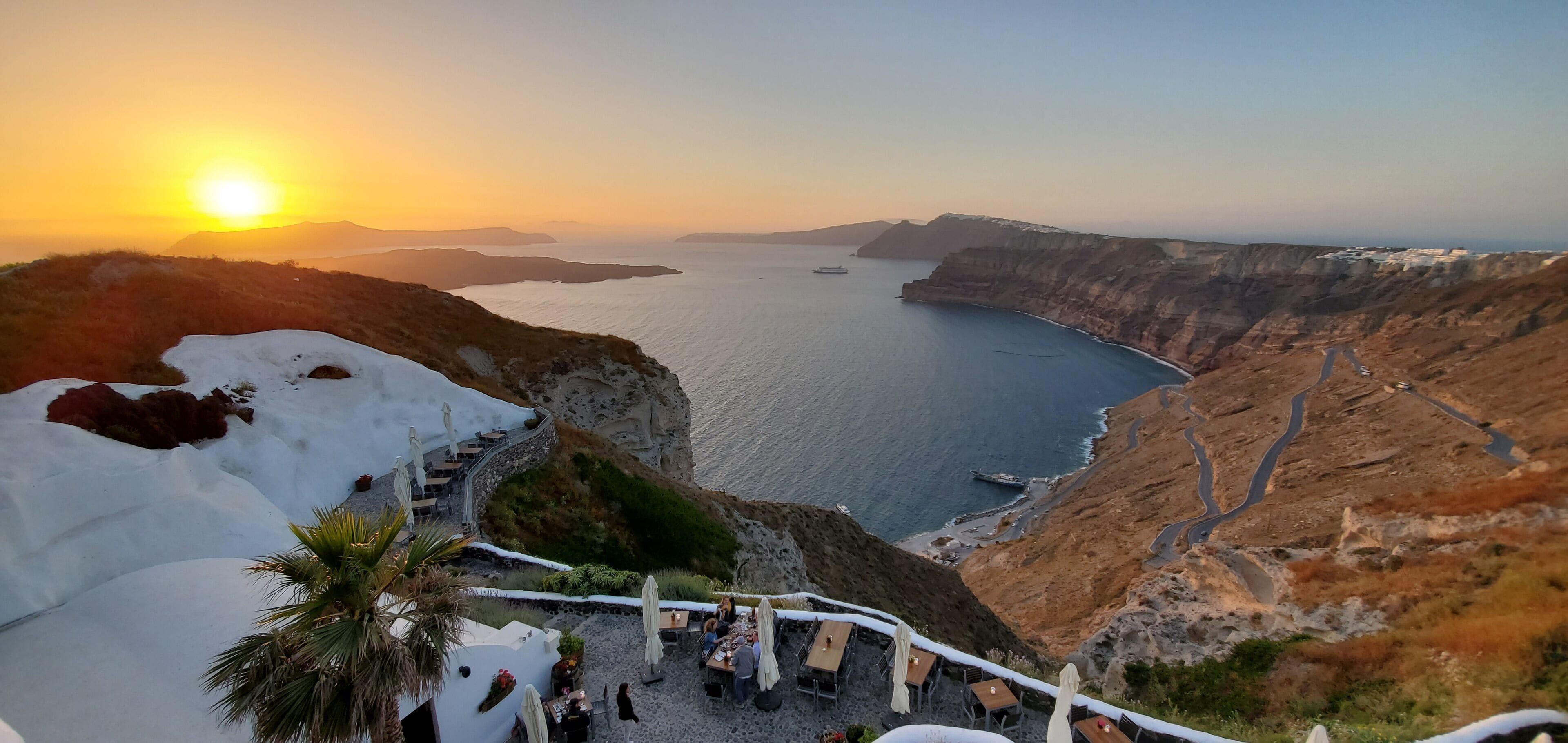 Un paisaje costero con un atardecer, acantilados y un restaurante con vistas al mar.