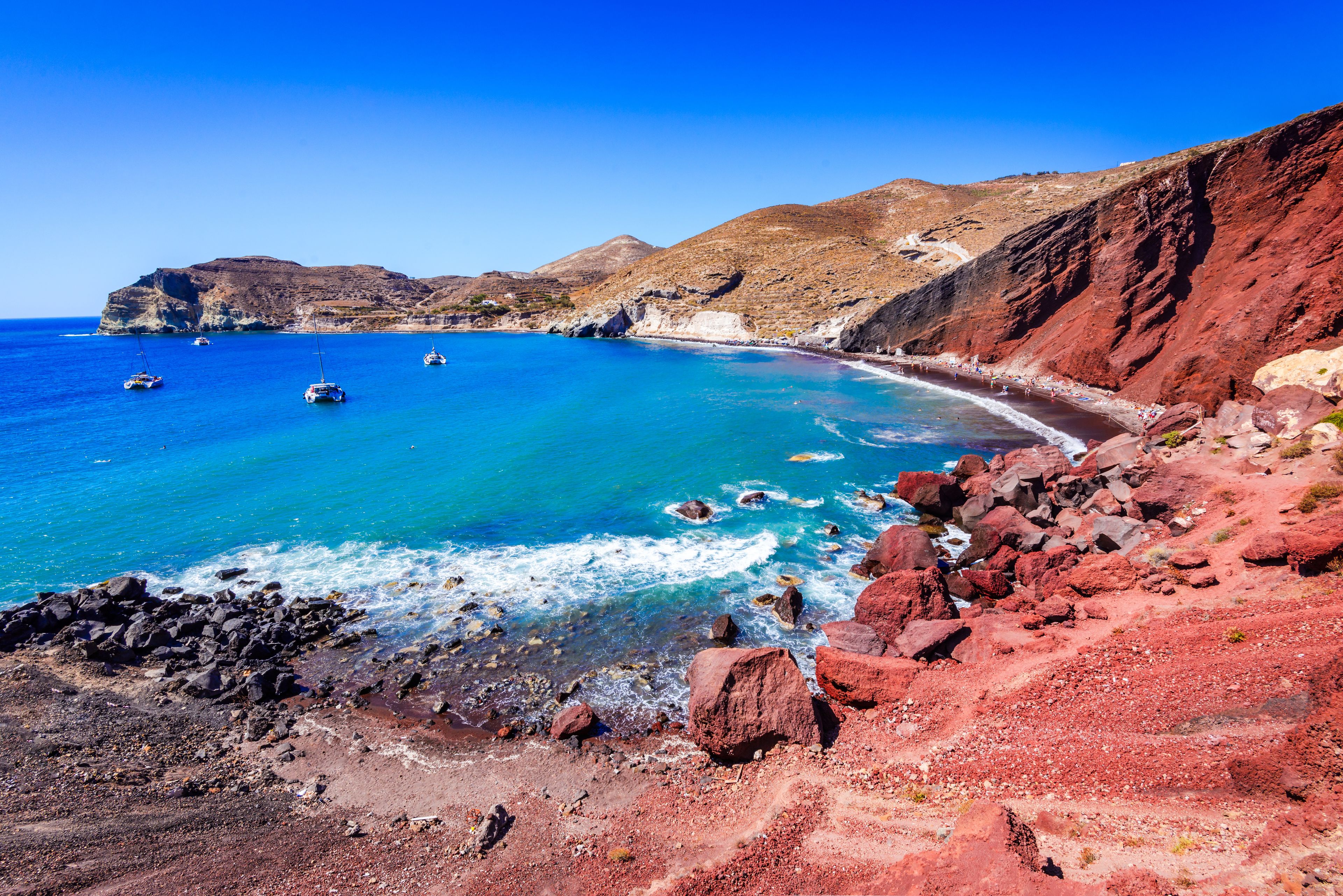 A coastal landscape with clear blue waters, rocky shores, and a mountainous backdrop.