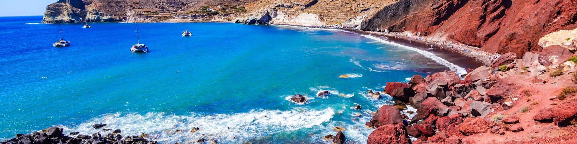 A coastal landscape with clear blue waters, rocky shores, and a mountainous backdrop.