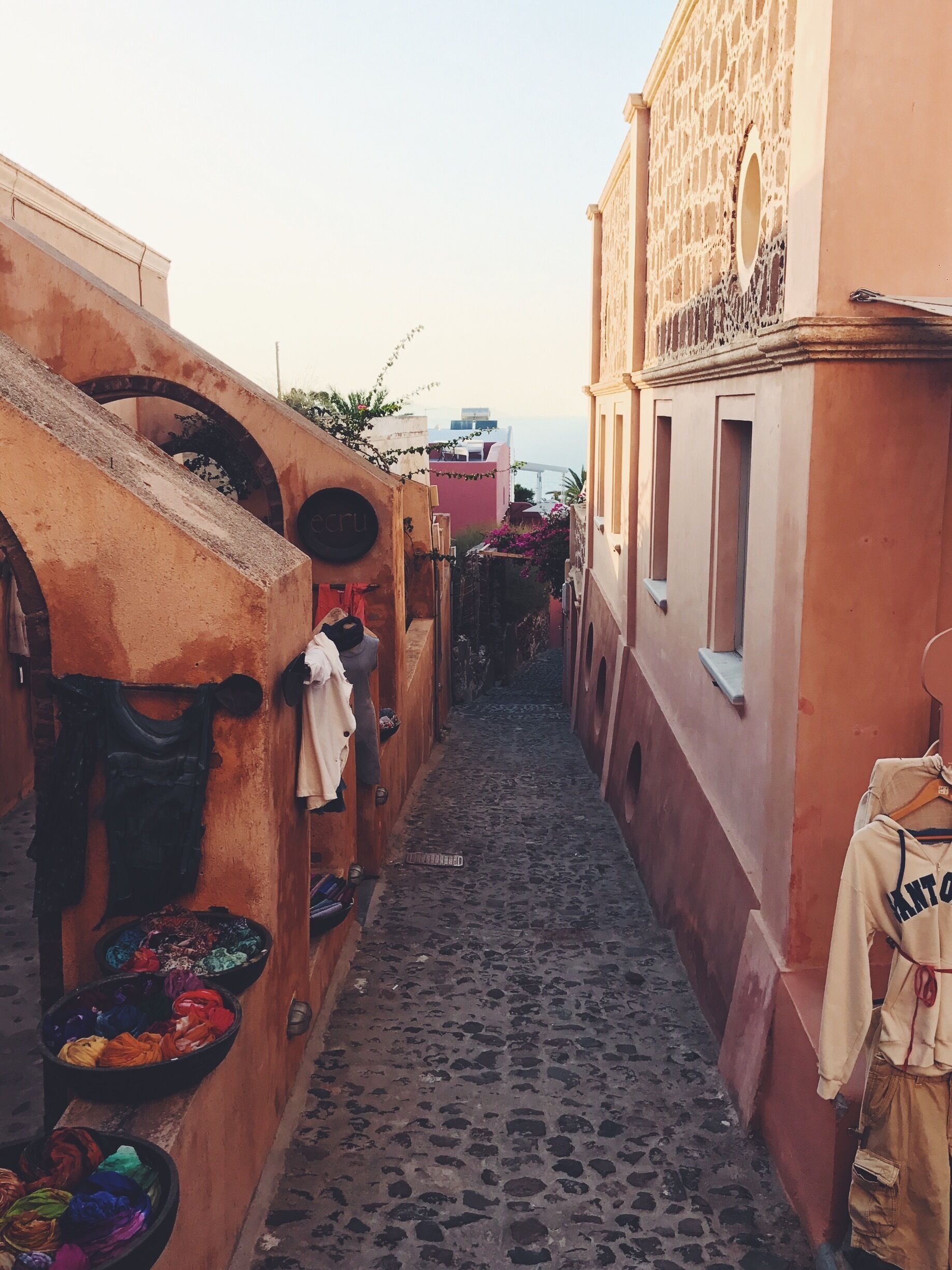 Um estreito beco de paralelepípedos ladeado por edifícios com portas em arco e roupa pendurada.