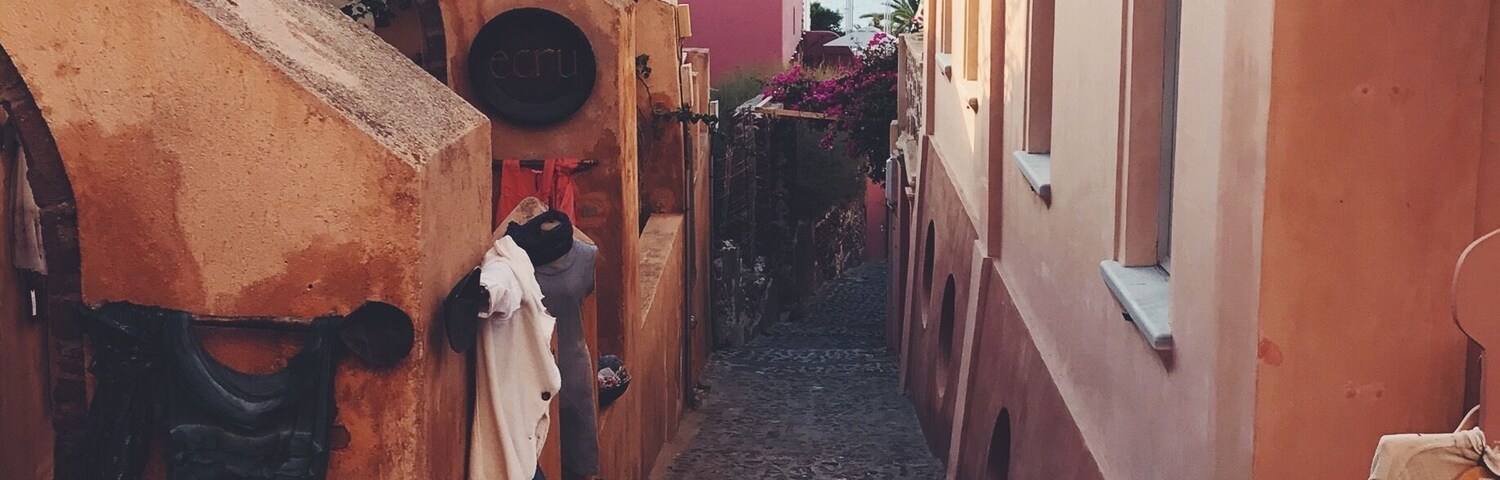 Um estreito beco de paralelepípedos ladeado por edifícios com portas em arco e roupa pendurada.