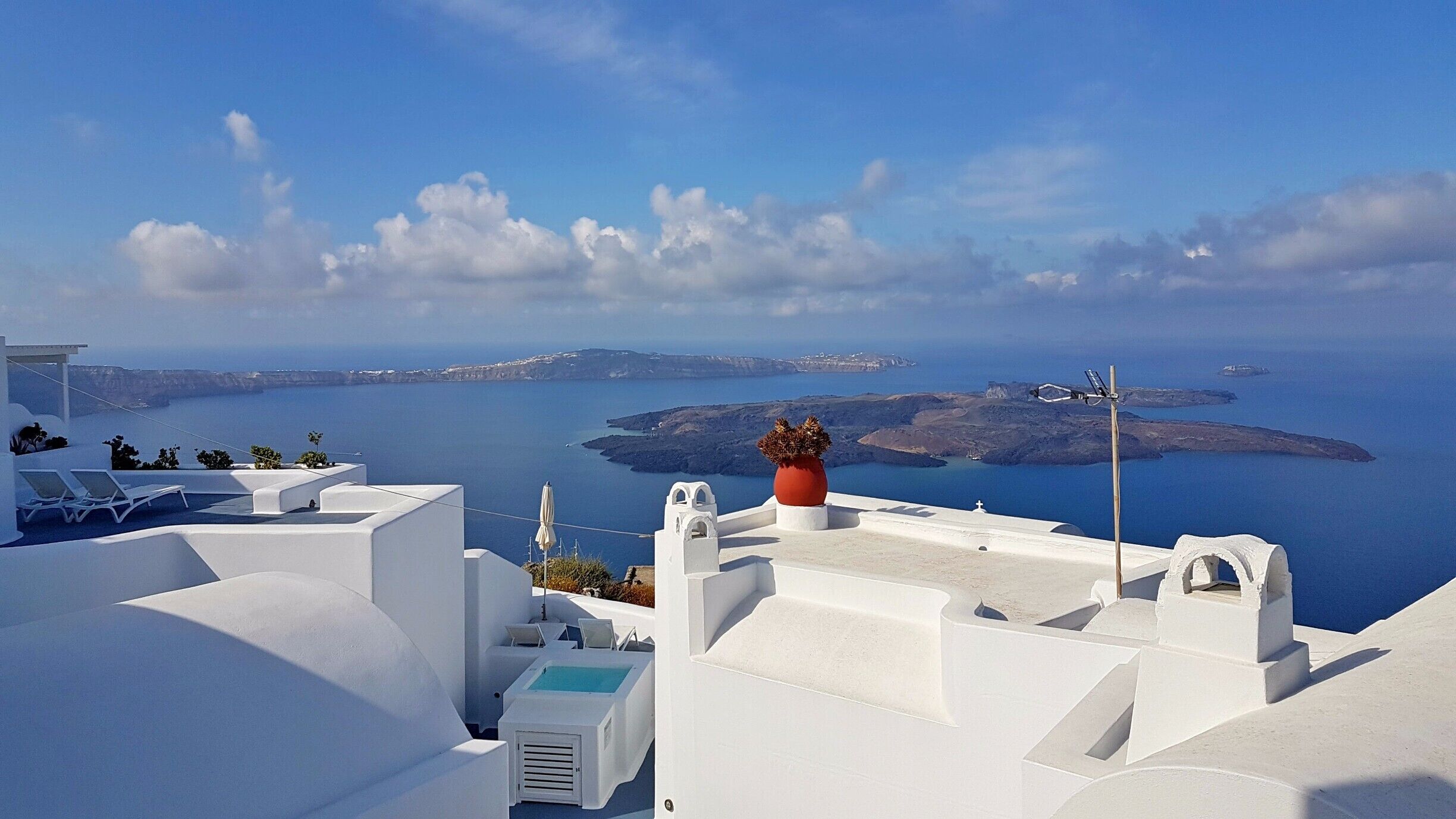 A white-washed building with a pool, overlooking a blue sea and islands.