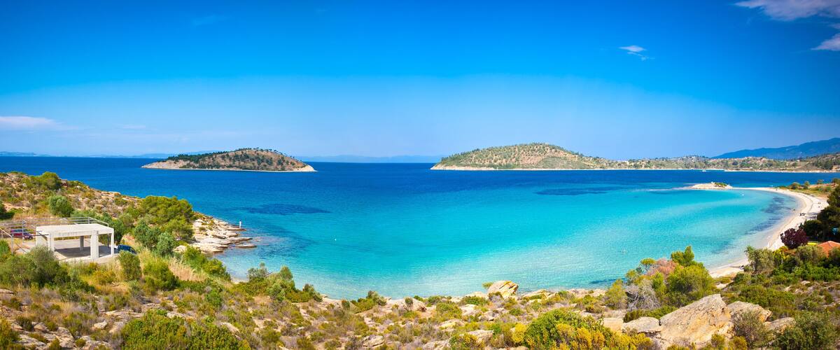A coastal landscape with clear turquoise waters, rocky shores, and two small islands.
