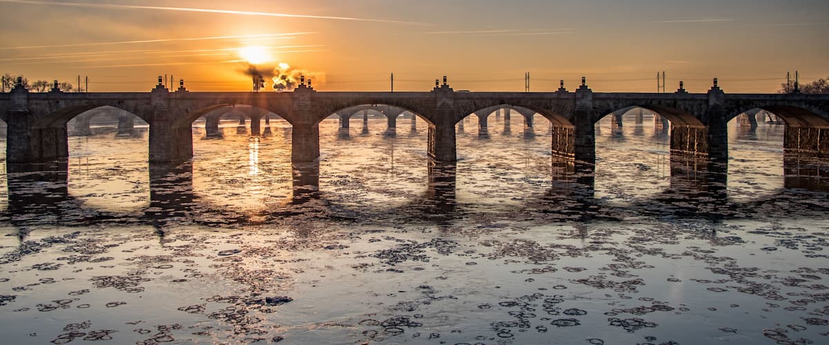 A stone bridge over water with the sun setting in the background.