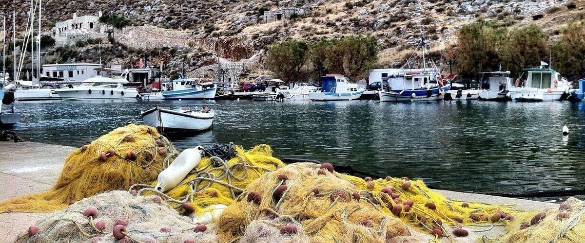 A harbor with boats, fishing nets, and a rocky hillside in the background.