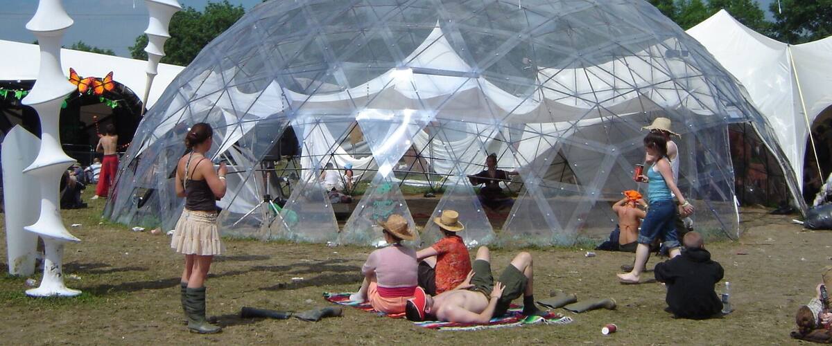 A large transparent geodesic dome structure surrounded by white, abstract sculptures and tents.