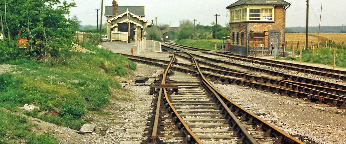 Railway tracks, a small station building, and a signal box in a rural setting.