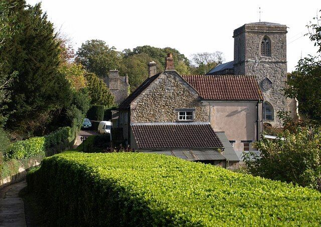 A stone church with a bell tower, surrounded by lush greenery and a pathway.