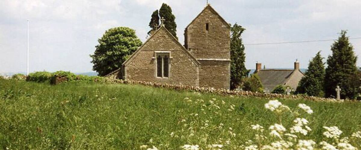 A stone church with a bell tower, surrounded by a grassy field and trees.