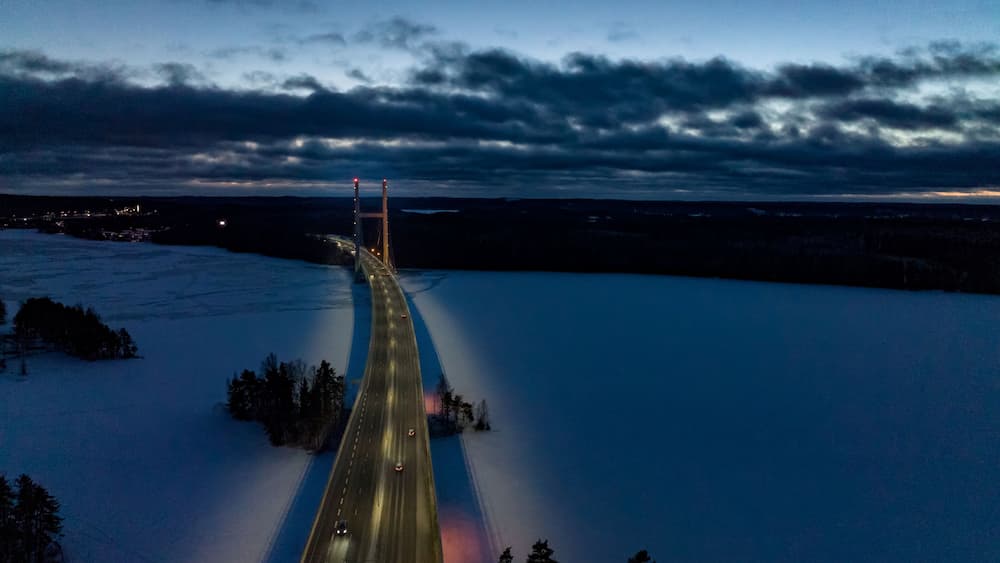 Eine schneebedeckte Brücke im Zwielicht, über die Fahrzeuge fahren.