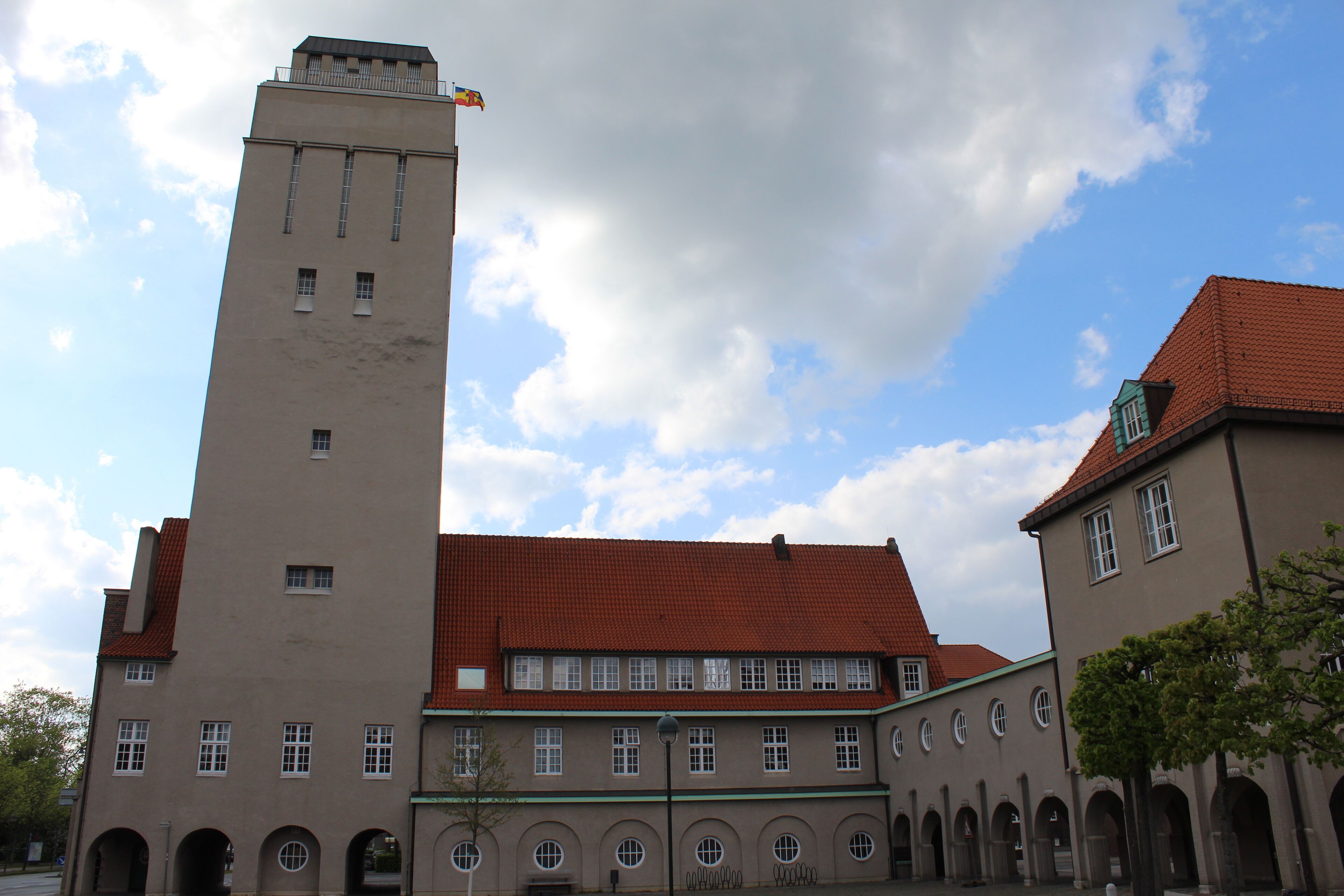 A historic building with a tall tower and red-tiled roof, surrounded by arched walkways.