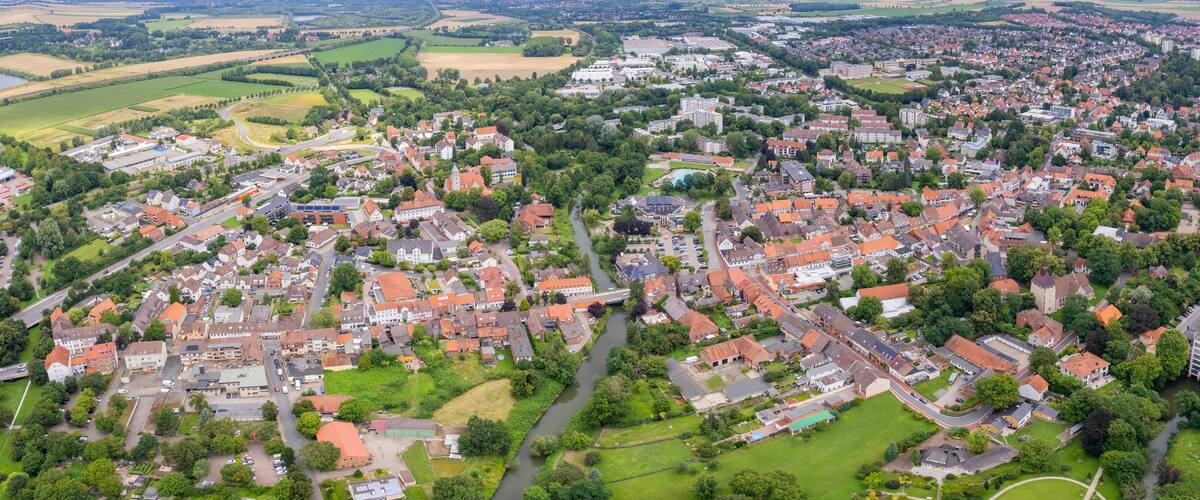 An aerial view of a town with a river running through it, surrounded by fields and greenery.