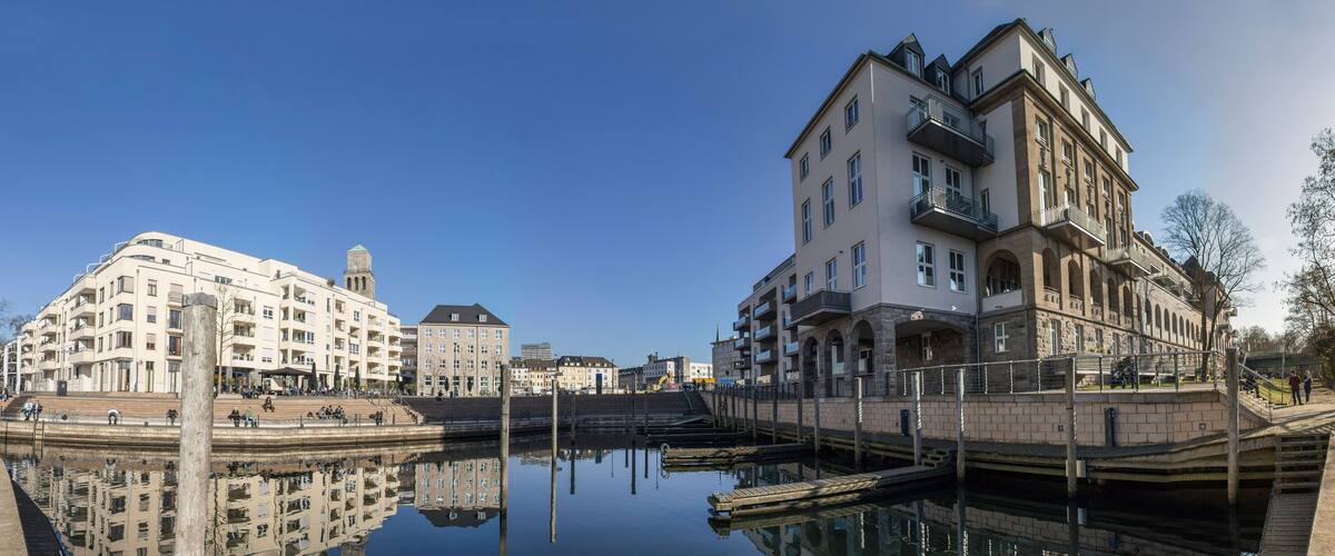 A riverside promenade with historic buildings, a bridge, and a calm water body reflecting the architecture.