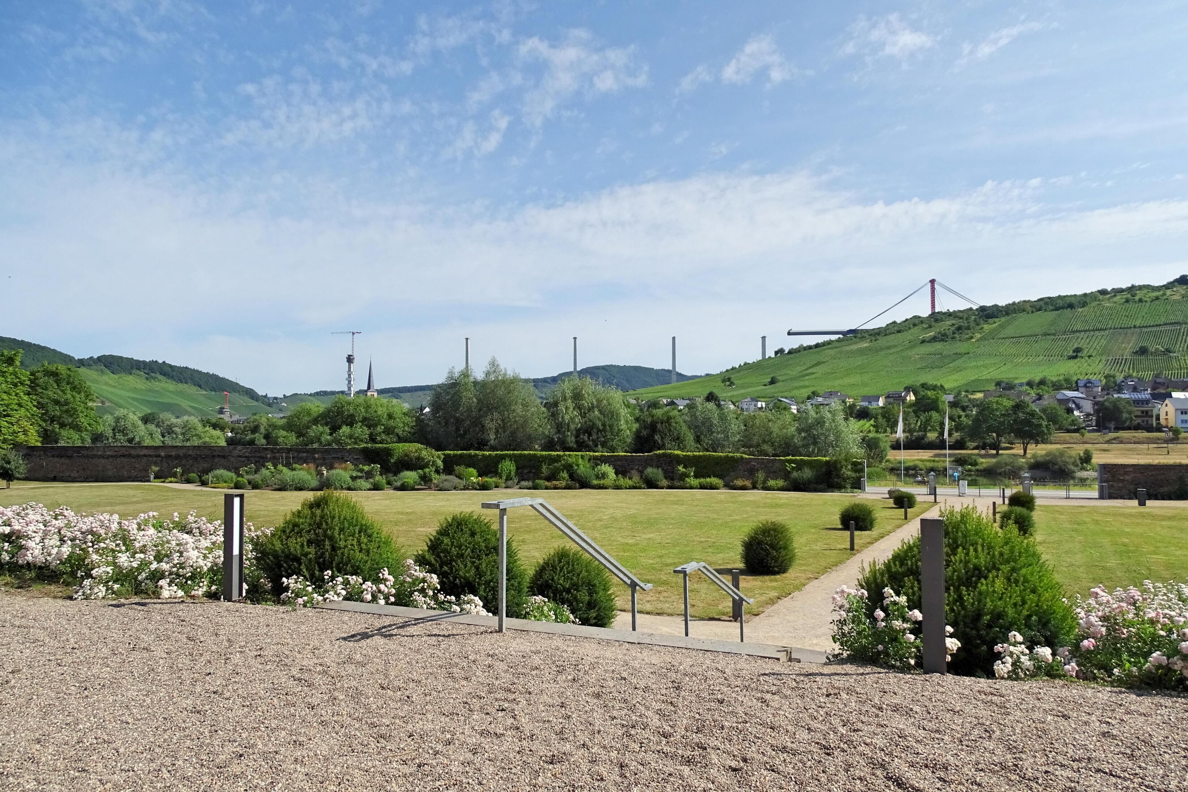 Un parque con un sendero de grava, barandillas metálicas y parterres de flores.