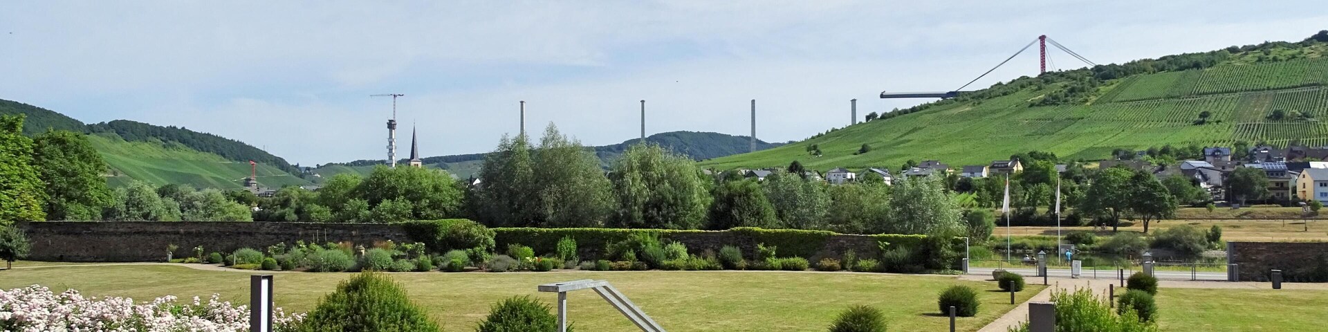Un parque con un sendero de grava, barandillas metálicas y parterres de flores.
