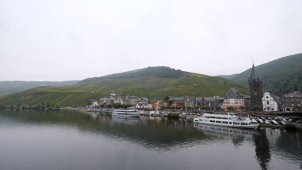 A river with a boat, a town with historic buildings, and a hill with a church tower.
