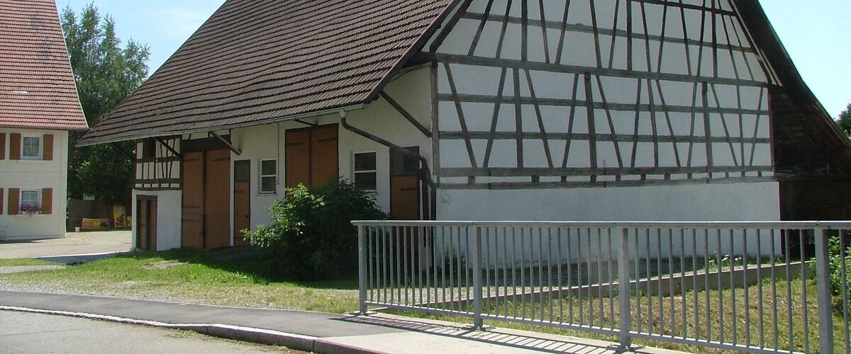 A traditional half-timbered house with a steeply pitched roof, a white fence, and a clear sky.