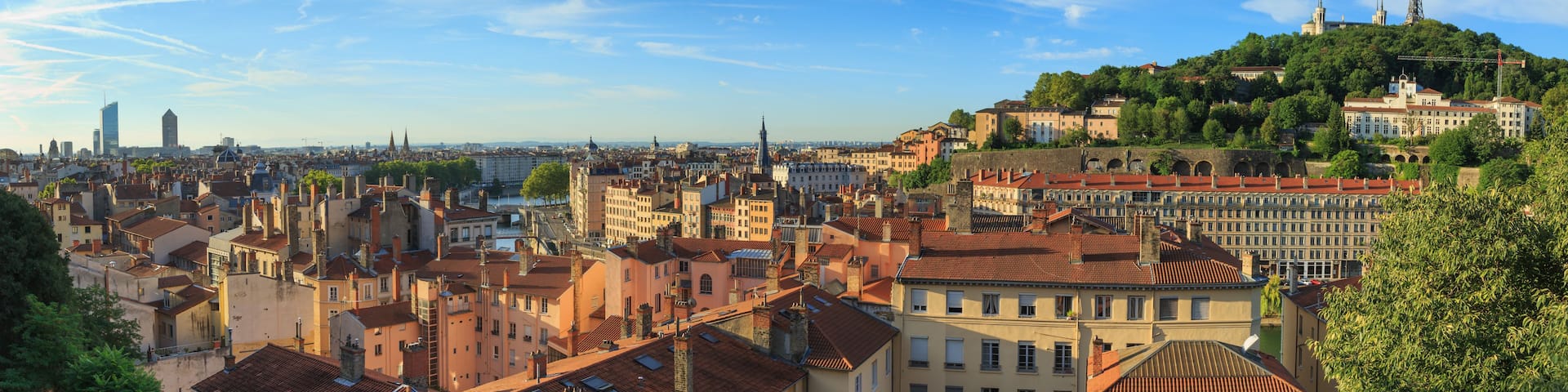 A panoramic view of a city with historic architecture, a prominent hilltop church, and a river in the foreground.