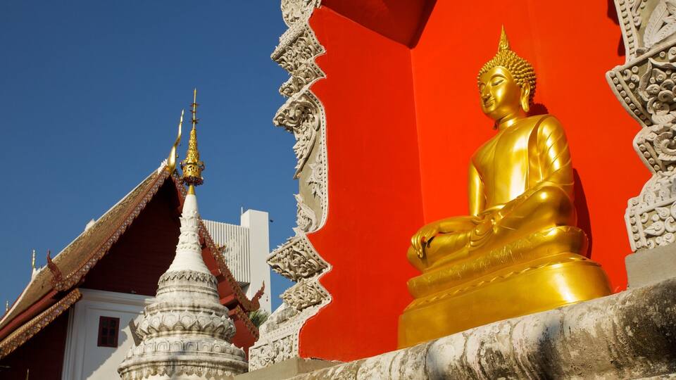 A golden Buddha statue in front of a red wall with intricate carvings.