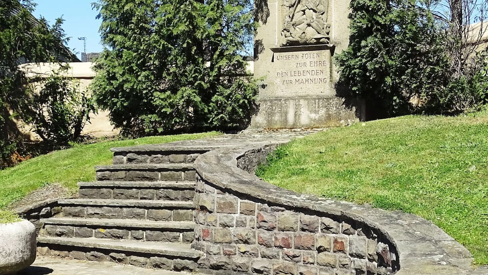 A stone staircase leading up to a monument with inscriptions, surrounded by grass and trees.