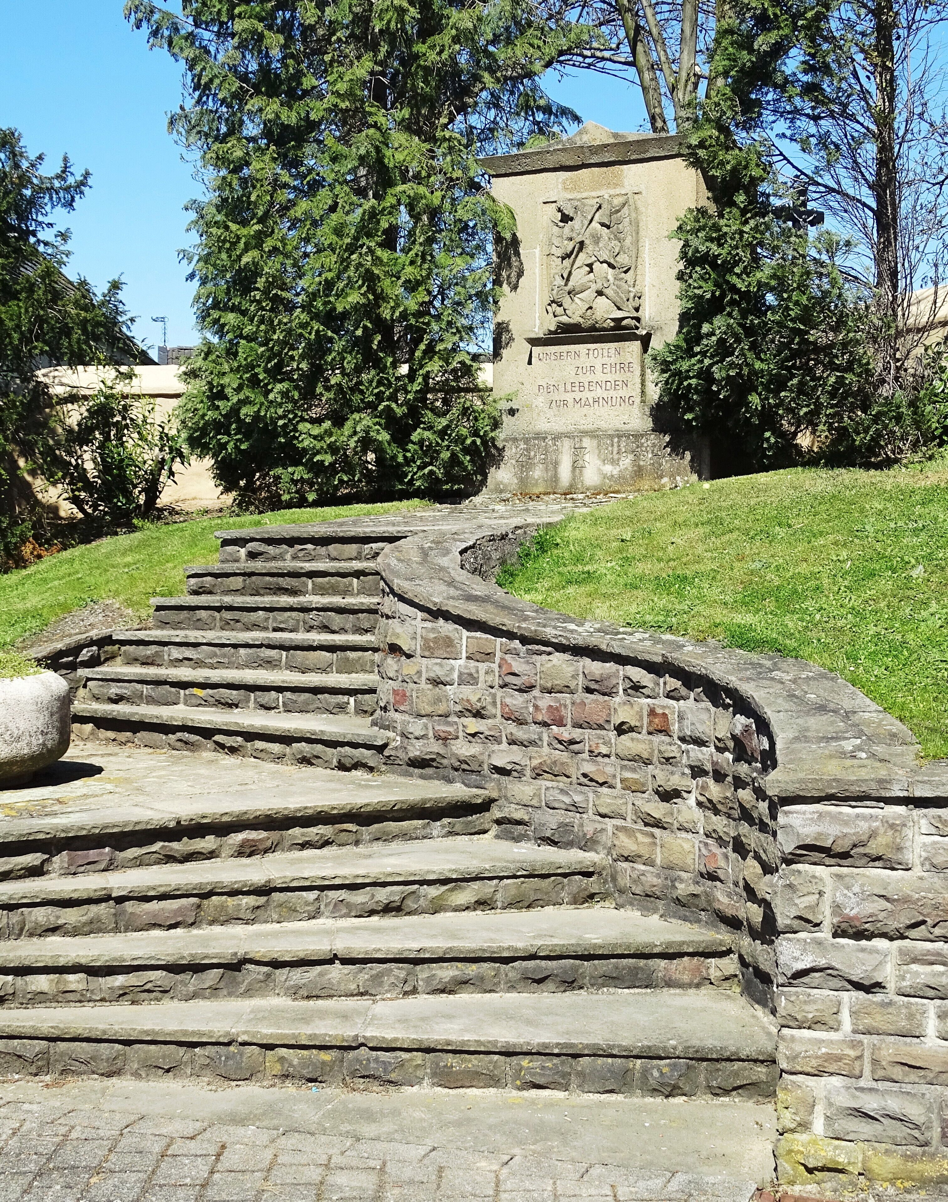 A stone staircase leading up to a monument with inscriptions, surrounded by grass and trees.