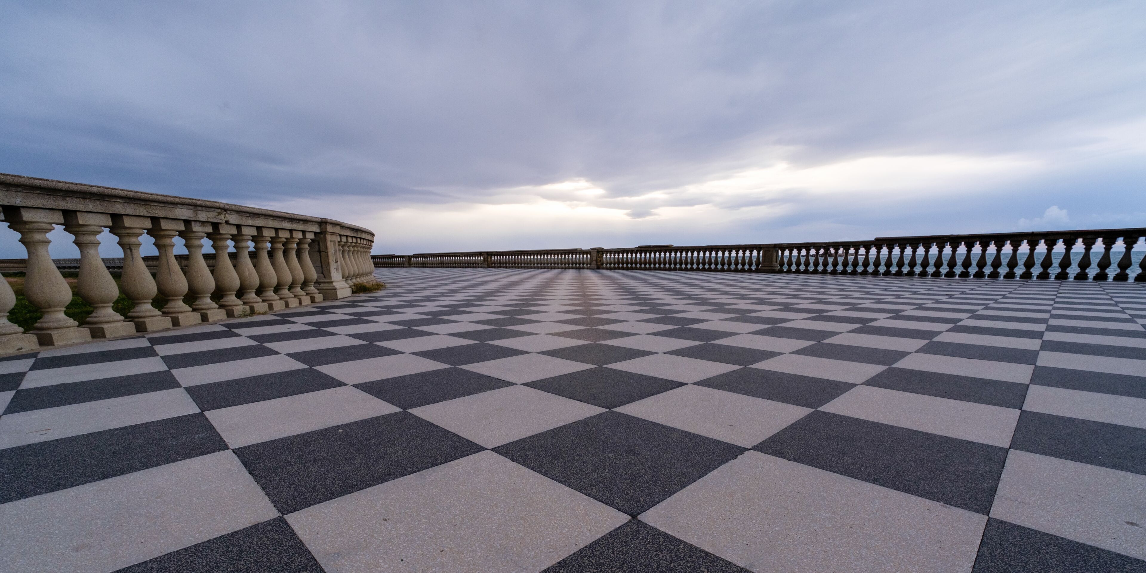 A checkered pavement leading to a wooden pier extending into the water.