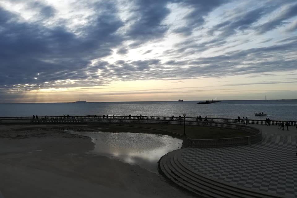 Un paseo marítimo costero con pavimento a cuadros, un mar tranquilo y una puesta de sol.