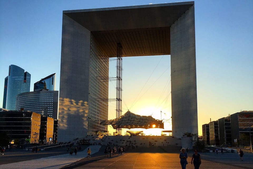 Un'ampia struttura in cemento con un'ampia apertura, circondata da edifici moderni e persone che camminano.