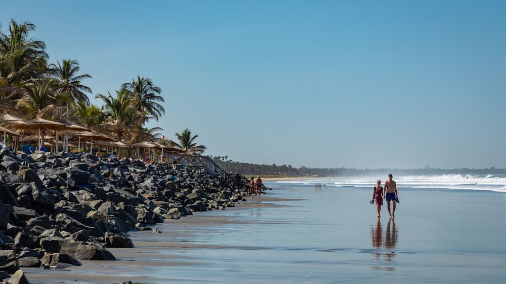 A beach with rocky shoreline, palm trees, and a clear sky.