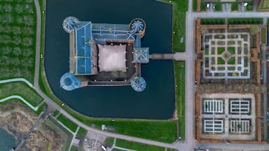 An aerial view of a large water body with a central building, surrounded by green areas and a formal garden layout.