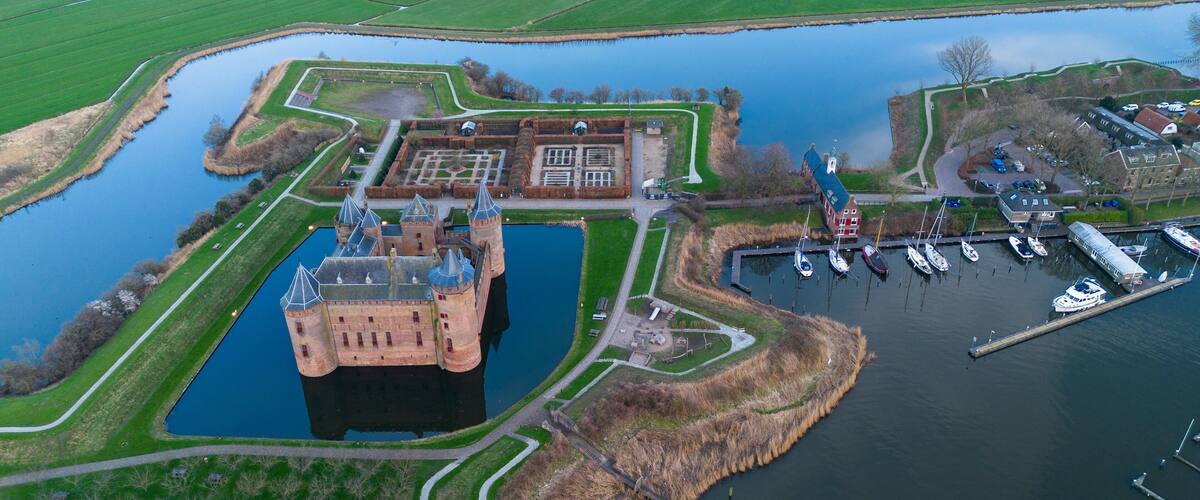 A castle surrounded by water, a marina with boats, and green fields.