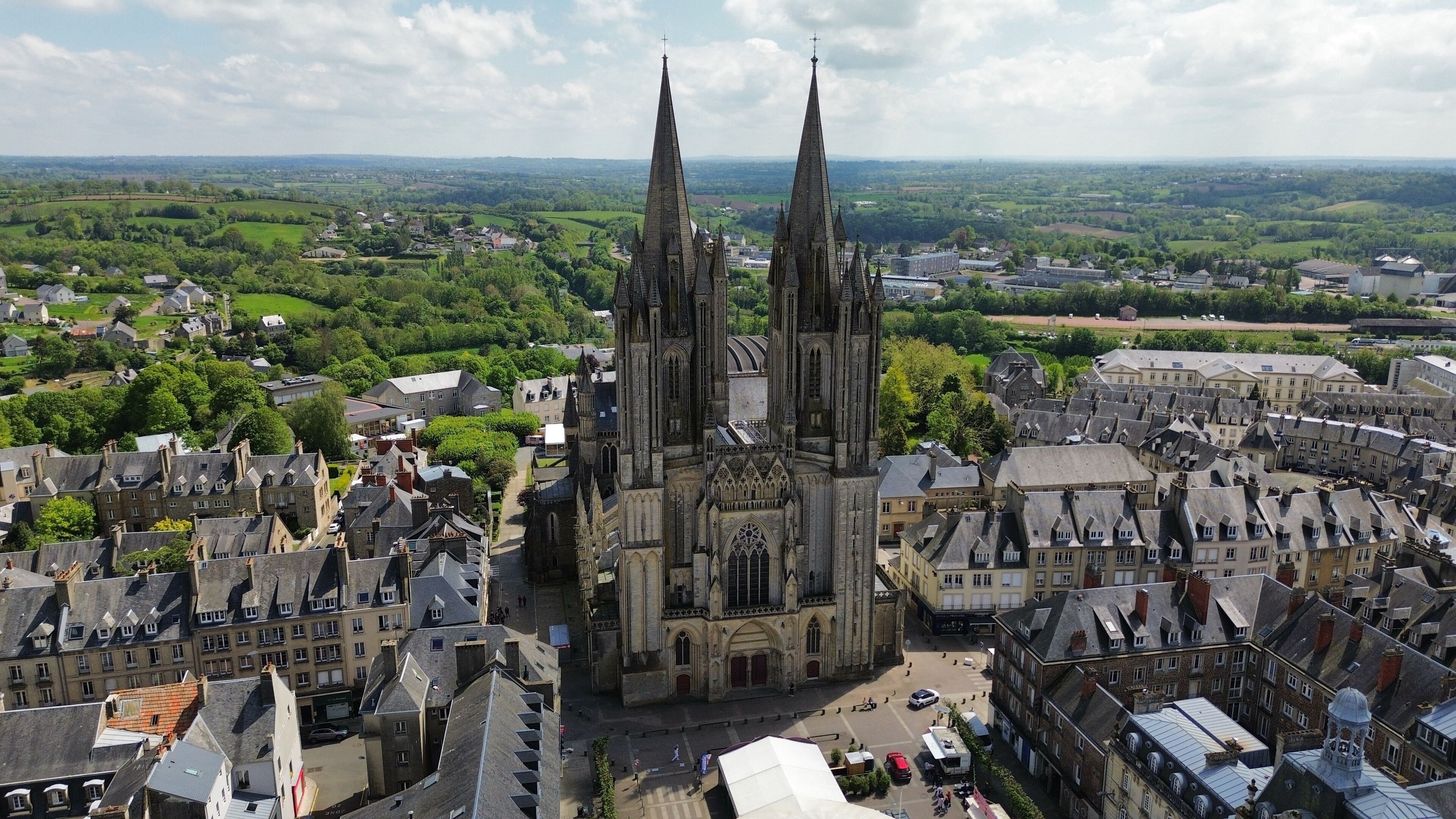 A cathedral with two tall spires, surrounded by historic buildings and a green landscape.